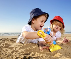 Gorgeous brother and sister ages 4 and 2 have fun digging in the sand at the beach