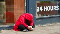 A young person sat on a street pavement curled up in a red hooded jacket and head bent right down. The shop window behind advertises 24 hours which would feel like an eternity when you are in crisis .