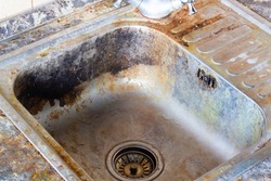 Very dirty kitchen sink. Detergents for the cooking room. The kitchen and dishwashing area need to be cleaned with a cleaning agent. Cleaning the Kitchen Sink. Old faulty water faucet. Close-up