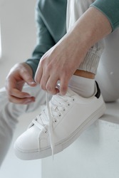 young guy sits and ties the laces on white sneakers