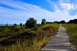 Long leading lines are created by the narrow boardwalk through the sand dunes at Kohler Andrea Park in Wilson and Sheboygan Wisconsin area with beautiful clouded skies in the late summer afternoon.