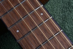 Selective focus on small twelfth fret marker dot on a walnut board. Tight focus includes sections position indicators of the steel E and A strings D and G Strings B and E Strings. 