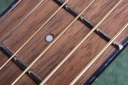 Selective focus on small fifth fret indicator marker dot on a walnut board. Tight focus includes small sections of the steel E and A strings D and G strings B and High E strings. 