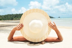 Girl lies on the white sand on the beach. Woman tanning relaxing on beach. Female adult from the back lying down with straw hat sunbathing under the tropical sun