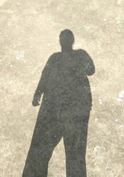Dark shadow of person standing on the ground outdoors in the sunlight, horror background