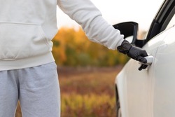 A man in a white sweater and black gloves opens the car door to steal him on a warm autumn day. Selective focus. Close-up