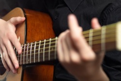 The hands of a young musician playing an acoustic guitar with metal strings close-up with a blurred background. selective focus
