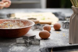 Rolled out puff pastry and molds for baking cookies, eggs, wooden rolling pin, spilled flour, a jug with ears of wheat on a black table in the kitchen. selective focus