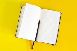 Open blank notebook and black pencil on yellow and blue background, white pages close up, school and work supply on desk, copy space empty book for notes and writing