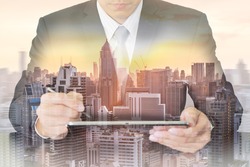 Double exposure of businessman working with tablet, cityscape and sunset as telecommunication and technology concept.