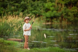 child boy engaged in fishing hobbies. he stands on the riverbank in the summer and holds a fishing rod with caught fish