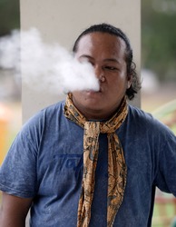Indonesian man wearing a scarf blowing her cigarette smoke  