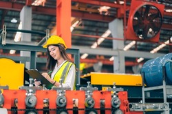 Happy professional beautiful Asian woman industrial engineer,worker,technician with safety hardhat use clipboard to inspect quality control of machinery in production steel manufacture factory plant