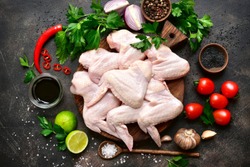 Raw chicken wings with ingredients for cooking on a wooden cutting board over dark slate or metal background.Top view .