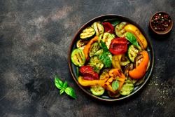Grilled vegetables (  colorful bell pepper, zucchini, eggplant ) with basil and dry herbs on a plate over dark slate, stone, concrete or metal background.Top view.