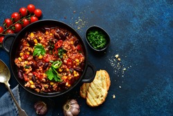 Chili con carne - traditional mexican minced meat and vegetables stew in tomato sauce in a cast iron pan on a dark blue slate, stone or concrete background. Top view with copy space.