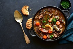 Beef bourguignon - meat stew with vegetables and mushrooms with red wine in a skillet over black slate, stone or concrete background , traditinal dish of french cuisine. Top view with copy space.