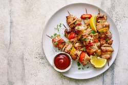 Chicken kebab skewers on a plate over light grey slate, stone or concrete background . Top view with copy space.