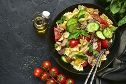 Tuna salad with pasta and vegetables in a black bowl on a dark slate,stone or concrete background.Top view.