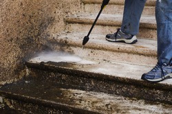 House maintenance : a manual worker cleans and defoams a dirty exterior stone staircase with the lance of a high-pressure washer, while the bad water, charged with moss, trikles down the steps