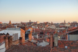 General view at sunrise over the tiled roofs of the old traditional houses of Toulouse historic city centre, in France, dominated by the ancient towers of Assézat, Jacobins, Bernuy and Saint-Sernin