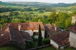 Houses with tiled roofs overhanging a verdant, hilly countryside landscape, as seen from the ramparts of Cordes-sur-Ciel, a rural town in the agricultural region of Albi, in the South of France
