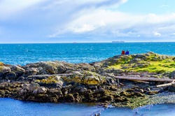 Faraway people sitting on a scenic rock outcropping enjoying a spectacular ocean view in Victoria, Vancouver Island, British Columbia, Canada 