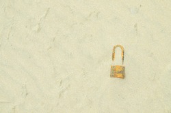 Hidden treasure on sand. The key is locked on the concrete floor. A  rusted padlock lies against a background of desert sand. 