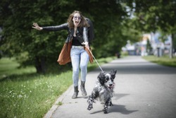 Young woman walking her dog on a street, having troubles holding him on a leash