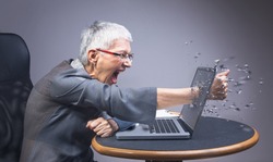 Crazy enraged senior business woman punching through her laptop, frustrated because it doesn't work properly
