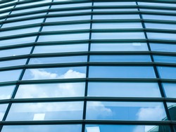 Close up transparent glass window panes on corporate office building reflecting blue sky and cloud