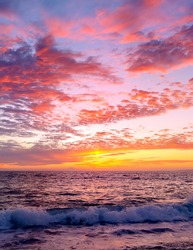 A Colorful Ocean Sunset Sky as a Gentle Wave Rolls to Shore in a Vertical Image Format