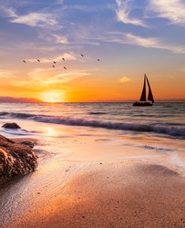 A Sailboat Sails Along The Ocean At Sunset In Vertical Image Format