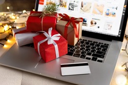 Christmas online shopping, sales and discounts promotions during the Christmas holidays, online shopping at home and lockdown coronavirus. Gifts and credit card on the laptop with blurred bokeh lights