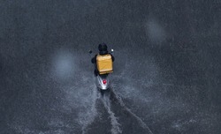 Delivery service from cafes and restaurants, courier on a scooter with a yellow backpack traveling through the puddles. The courier delivers food on a motorcycle. Fast food delivery to customers.