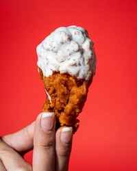 Hand holding a chicken wing with buffalo and ranch dressing on a red background.