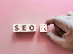 SEO concept on wooden cubes with magnifying glass against pink background.