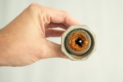Old calcified and clogged water pipe with brown rust held in hand by plumber