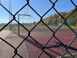 Blurred outdoor basketball court (streetball), seen from behind a metal chainlink fence.