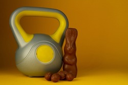 Kettlebell weight and chocolate Easter bunny. Healthy fitness lifestyle composition, gym workout and training fit concept. Cheat day temptation vs sticking to diet. Copy space on yellow background.