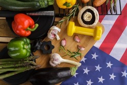 Gym dumbbells with healthy vegetables and flag of the United States of America. Fit barbecue party concept for Fourth of July Independence Day holiday celebration in USA. Fitness workout composition.
