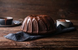 Delicious dessert, dark chocolate bundt cake topped with ganache glaze on rustic wooden background
