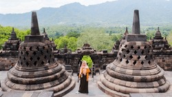 A beautiful woman in an orange dress poses at the Borobudur temple. The biggest temple in the world.