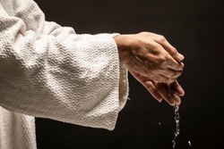 Water for Baptism pouring out of the hands of Jesus Christ during a dark night.
