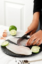 Female Hand Cutting Dori Fillet Pangasius Fish above Stone Board, Process Cooking in the Kitchen