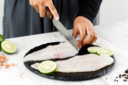 Female Hand Cutting Dori Fillet Pangasius Fish above Stone Board, Process Cooking in the Kitchen