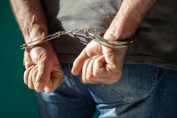 Detained man with hands behind his back. Cutaway view of a handcuffed man in jeans standing, human rights concept.