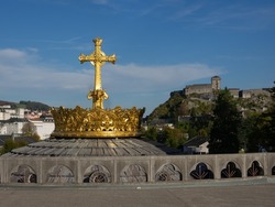 Crown of the cathedral of Lourdes, France. With a view of the castle in the background.