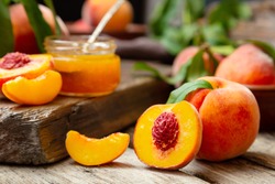 Peaches with leaves on dark wooden board with peach in halves with peach seed stone. Composition with ripe juicy peaches Harvest for food. Fresh organic fruit