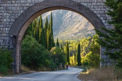 Picturesque archway at the entrance to Croatia from Montenegro. In the depths of the arch, slender cypresses grow along the road. Cyclists ride along the road